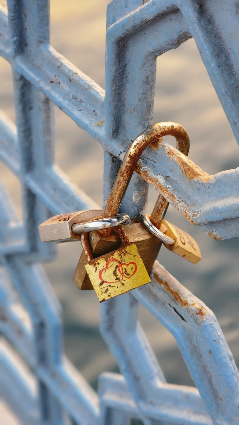 A rusty love padlock attached to a blue iron fence with heart symbol.
